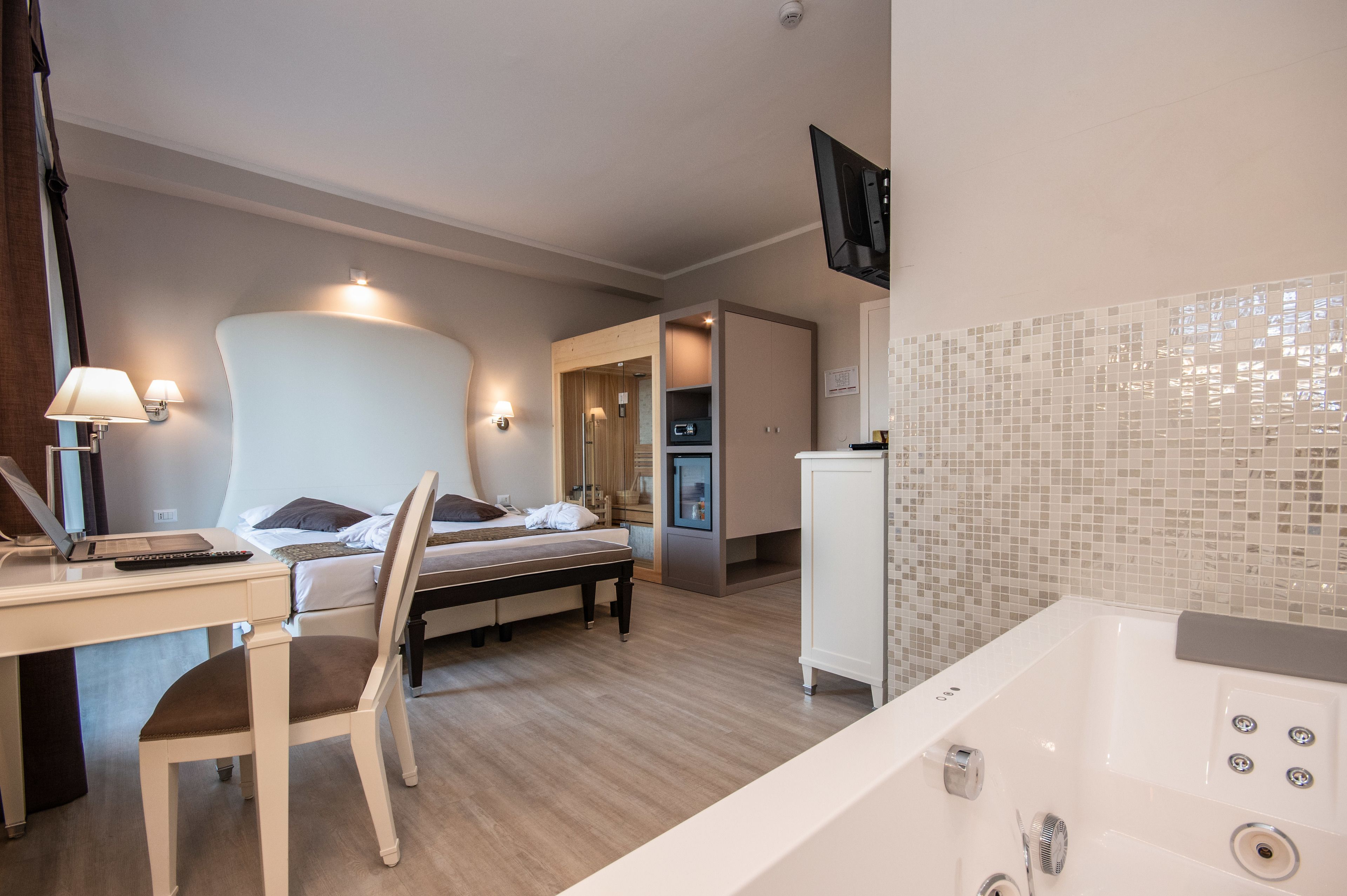 A modern hotel room with a bed, desk, chair, and a bathroom with a bathtub.