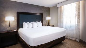 Habitación de hotel con una cama grande, dos mesitas de noche con lámparas, una alfombra estampada y un diseño geométrico en la pared.