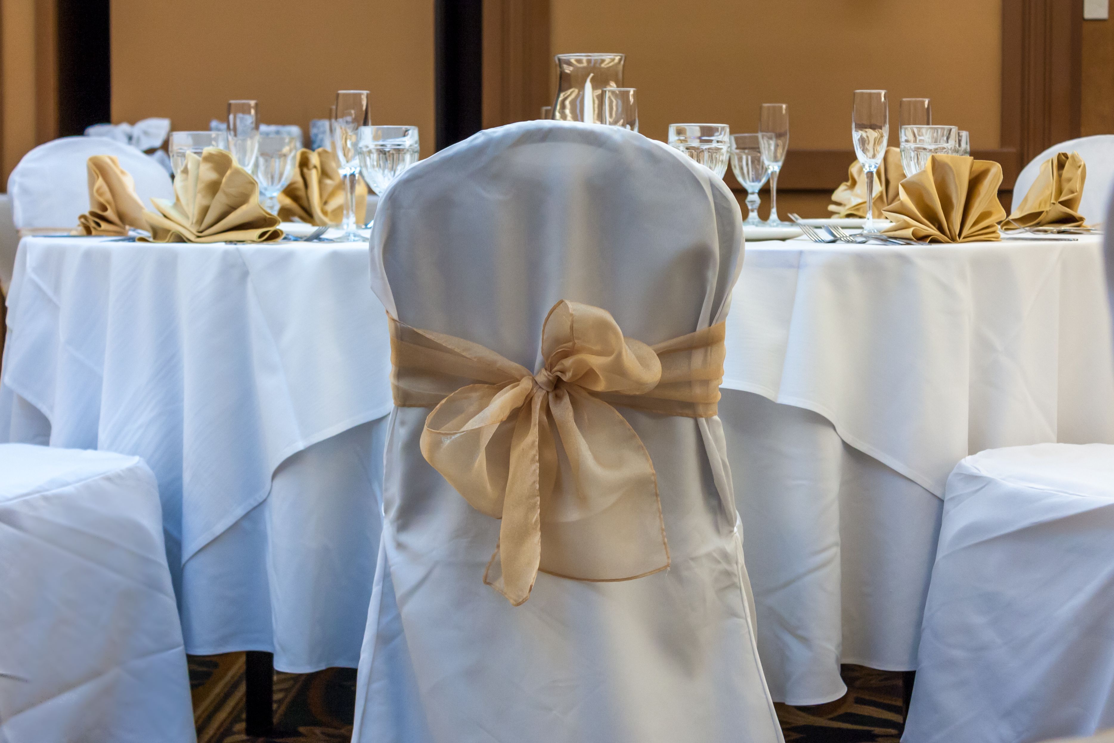 A banquet hall with round tables covered in white tablecloths, each with gold napkins tied in bows.