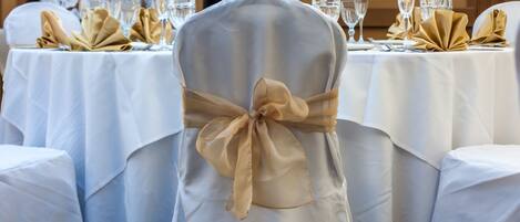 A banquet hall with round tables covered in white tablecloths, each with gold napkins tied in bows.