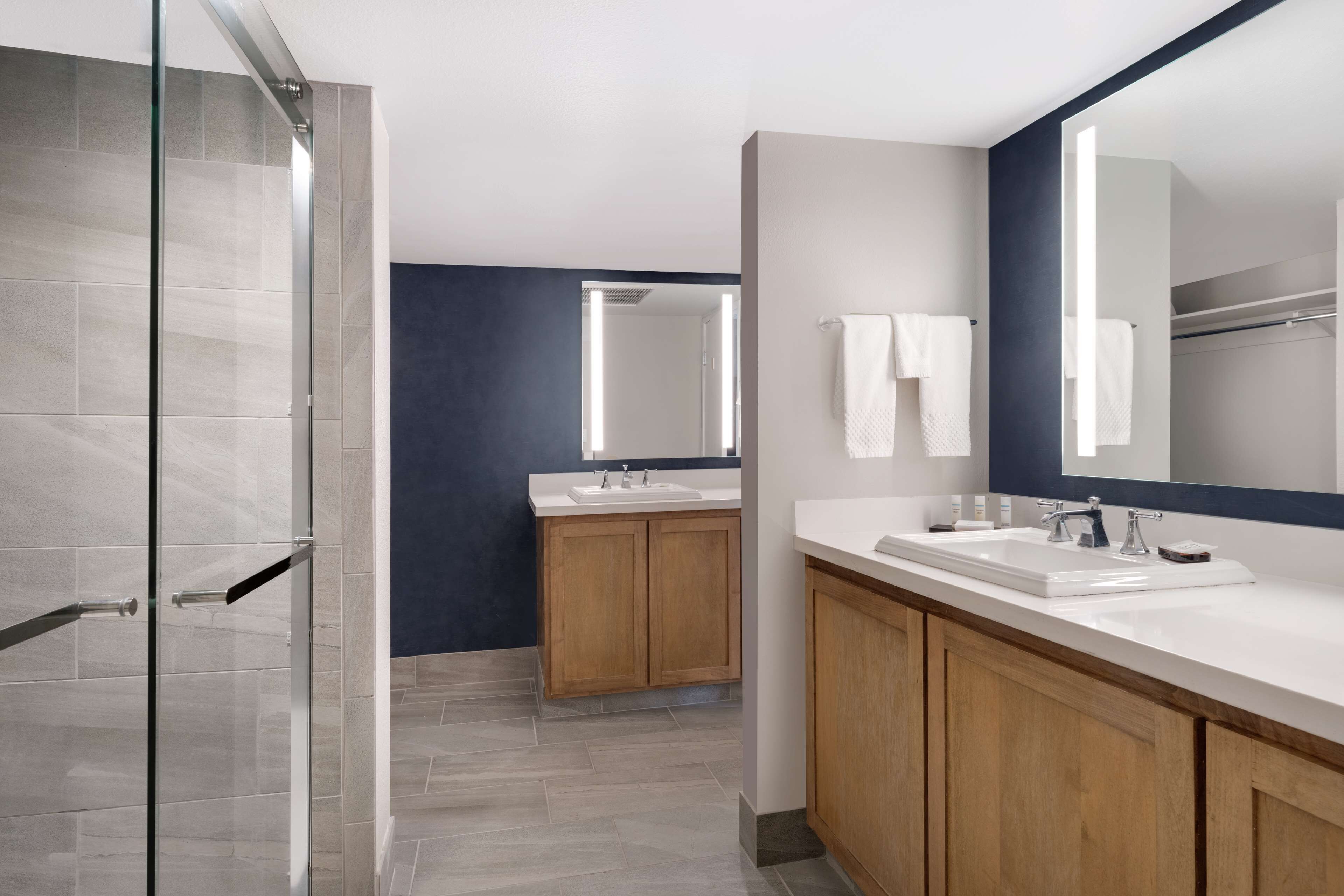 Une salle de bain moderne avec une douche à parois de verre, des meubles en bois et un grand miroir.