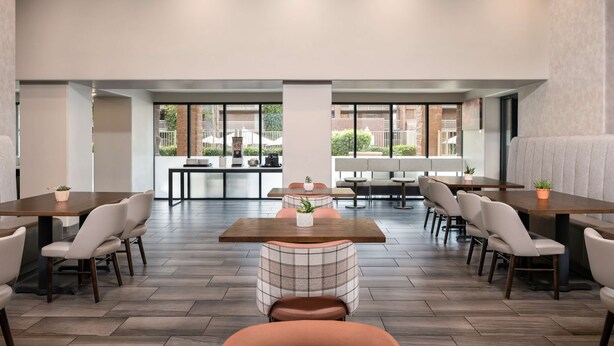 A spacious indoor area with multiple seating arrangements, including tables and chairs, and large windows providing views of the outside.