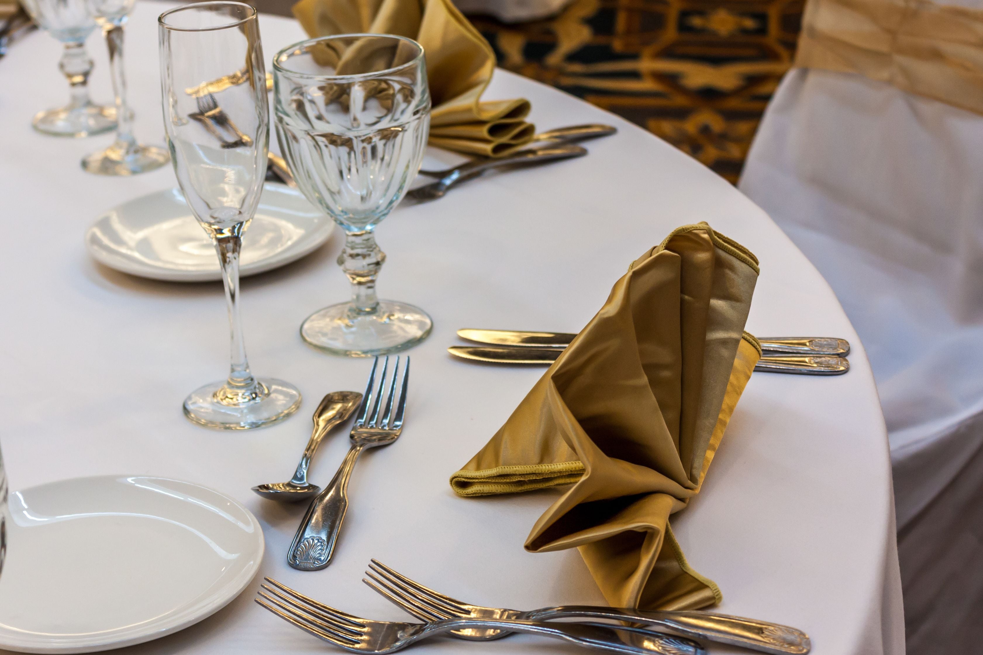 A table set with white plates, gold napkins, and silverware.