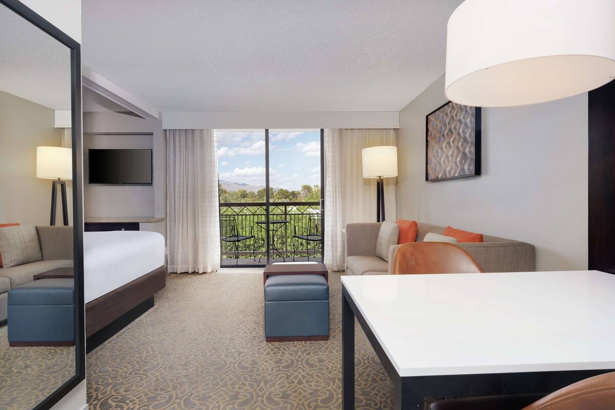A hotel room with a bed, a sofa, a desk, and a balcony with a view.