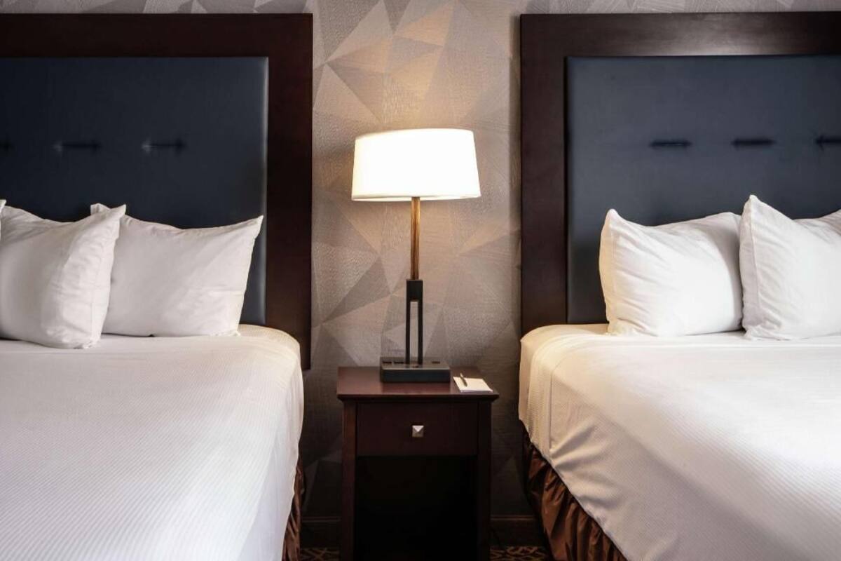 A hotel room with two beds, a nightstand with a lamp, and a geometric-patterned wall.