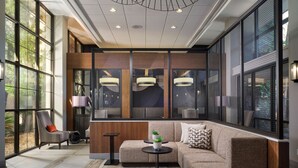 A modern interior with a sectional sofa, a small round table, and a chair. There are large windows with a view of greenery outside.