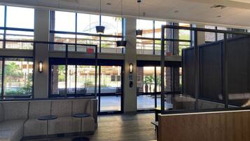 A spacious lobby with a modern design, featuring a seating area with sofas and small tables, large windows offering views of the outdoors, and a high ceiling with recessed lighting.