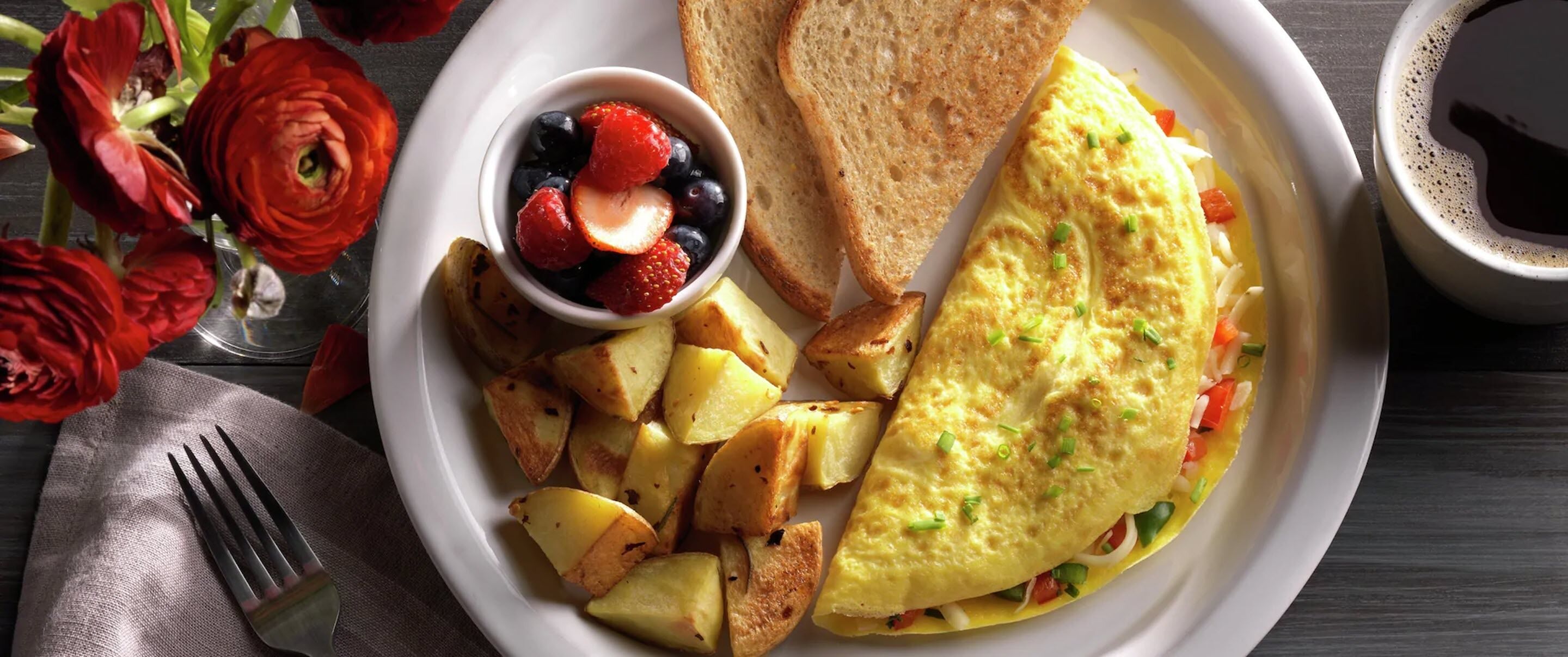 Une assiette de petit-déjeuner comprenant une omelette, des toasts, des pommes de terre rôties et une portion de fruits rouges.