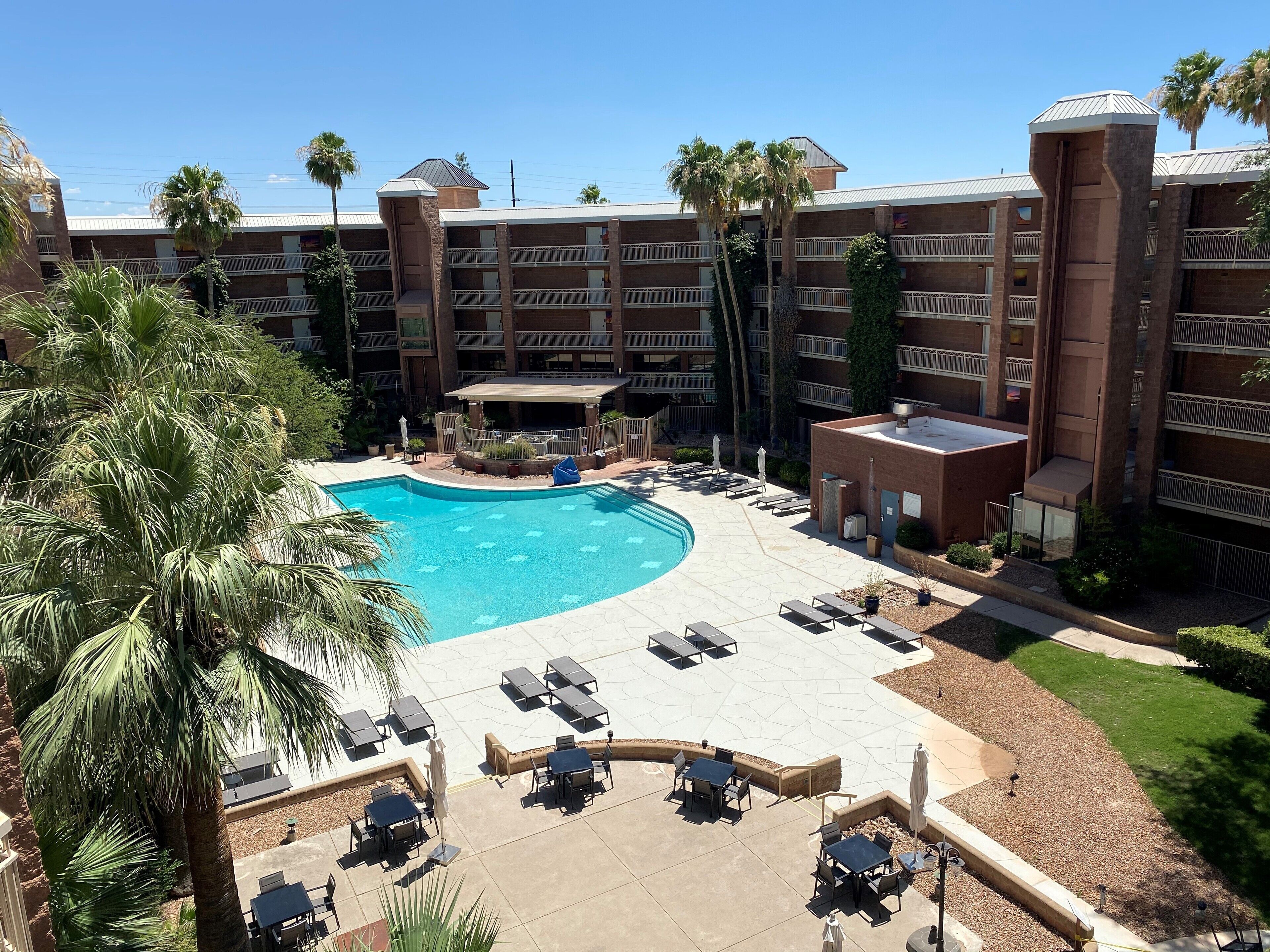 A hotel with a swimming pool, outdoor seating, and palm trees.