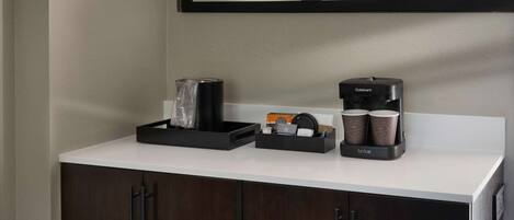 A modern bathroom with a white countertop, a black coffee maker, and a Cuisinart espresso machine.