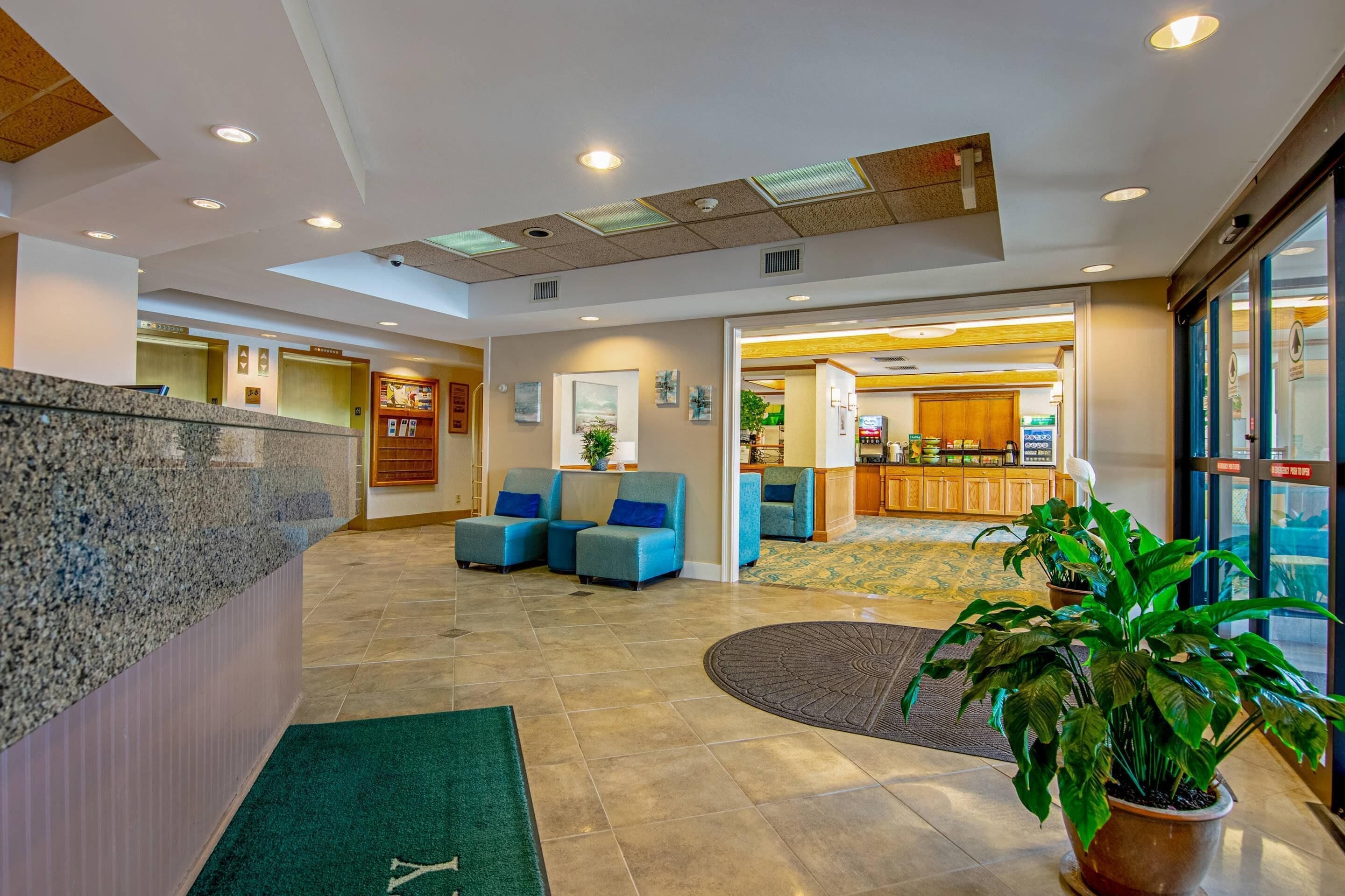 A hotel lobby with a reception desk, seating area, and a view of the kitchen in the background.