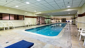 An indoor swimming pool with tiled flooring, a blue pool area, and white chairs around the perimeter.