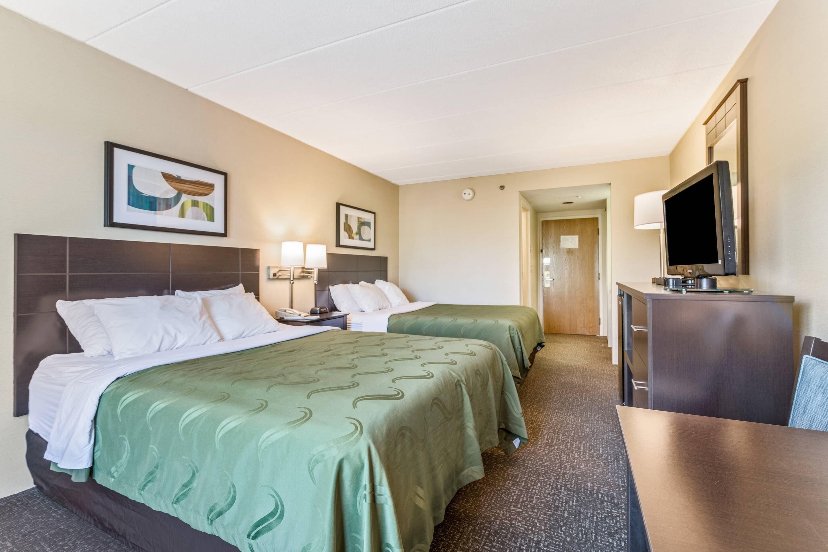 A hotel room with two beds, a desk, a TV, and a door leading to a bathroom.