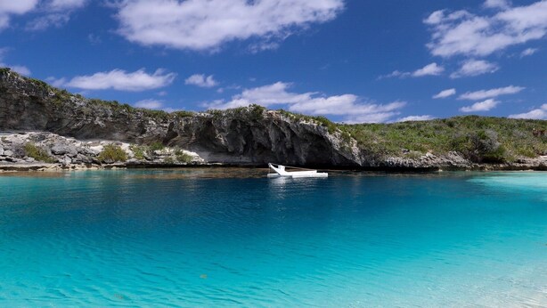 A clear turquoise sea, sandy beach, and rocky cliffs under a blue sky with clouds. - Stella Maris Resort Club (Stella Maris)