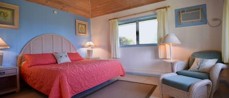 A bedroom with a bed, two nightstands, a chair, a window with curtains, and wall-mounted air conditioning.