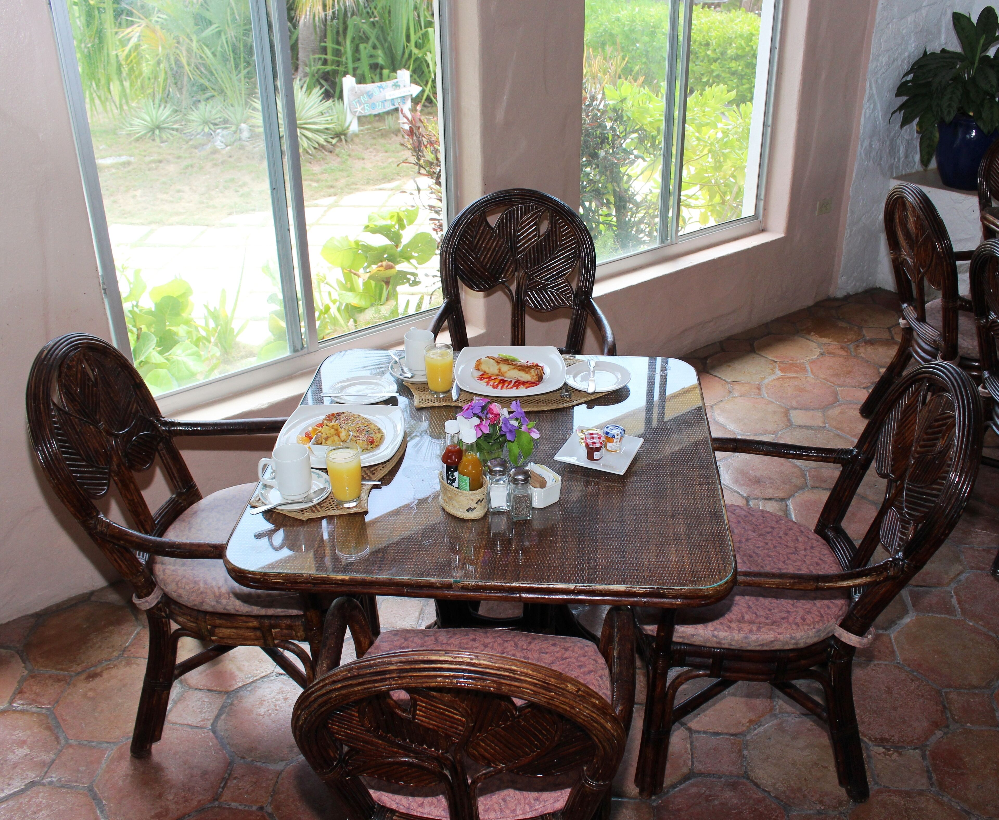A dining table with plates, glasses, and condiments, surrounded by wicker chairs.