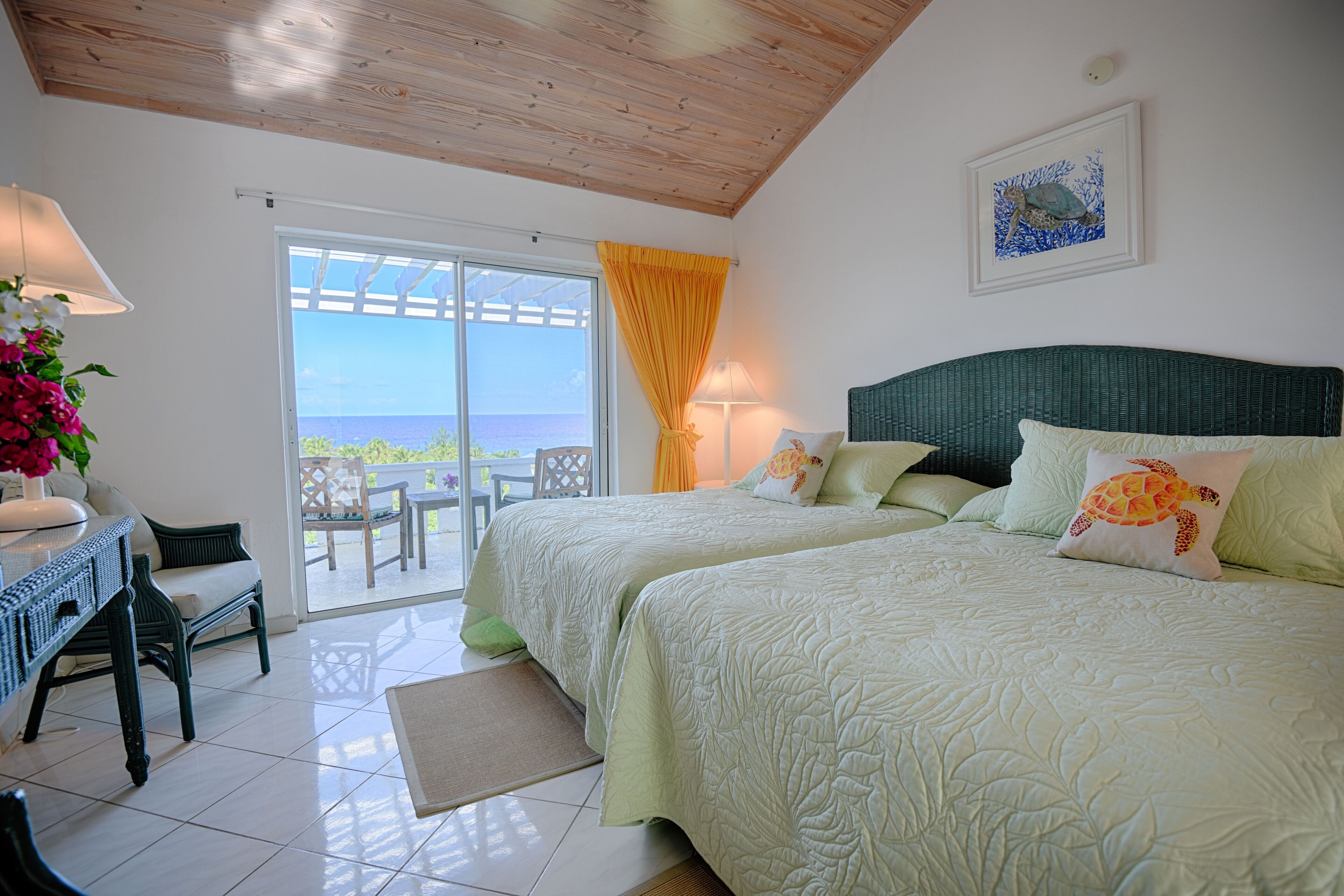 A bedroom with two beds, a view of the sea through a glass door, a wooden ceiling, and a painting on the wall.