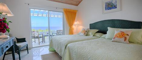 A bedroom with two beds, a view of the sea through a glass door, a wooden ceiling, and a painting on the wall.
