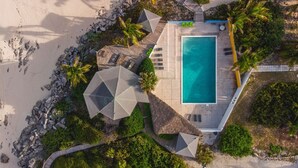 An aerial view of a resort with a swimming pool, thatched-roof structures, and palm trees. - Stella Maris Resort Club (Stella Maris)