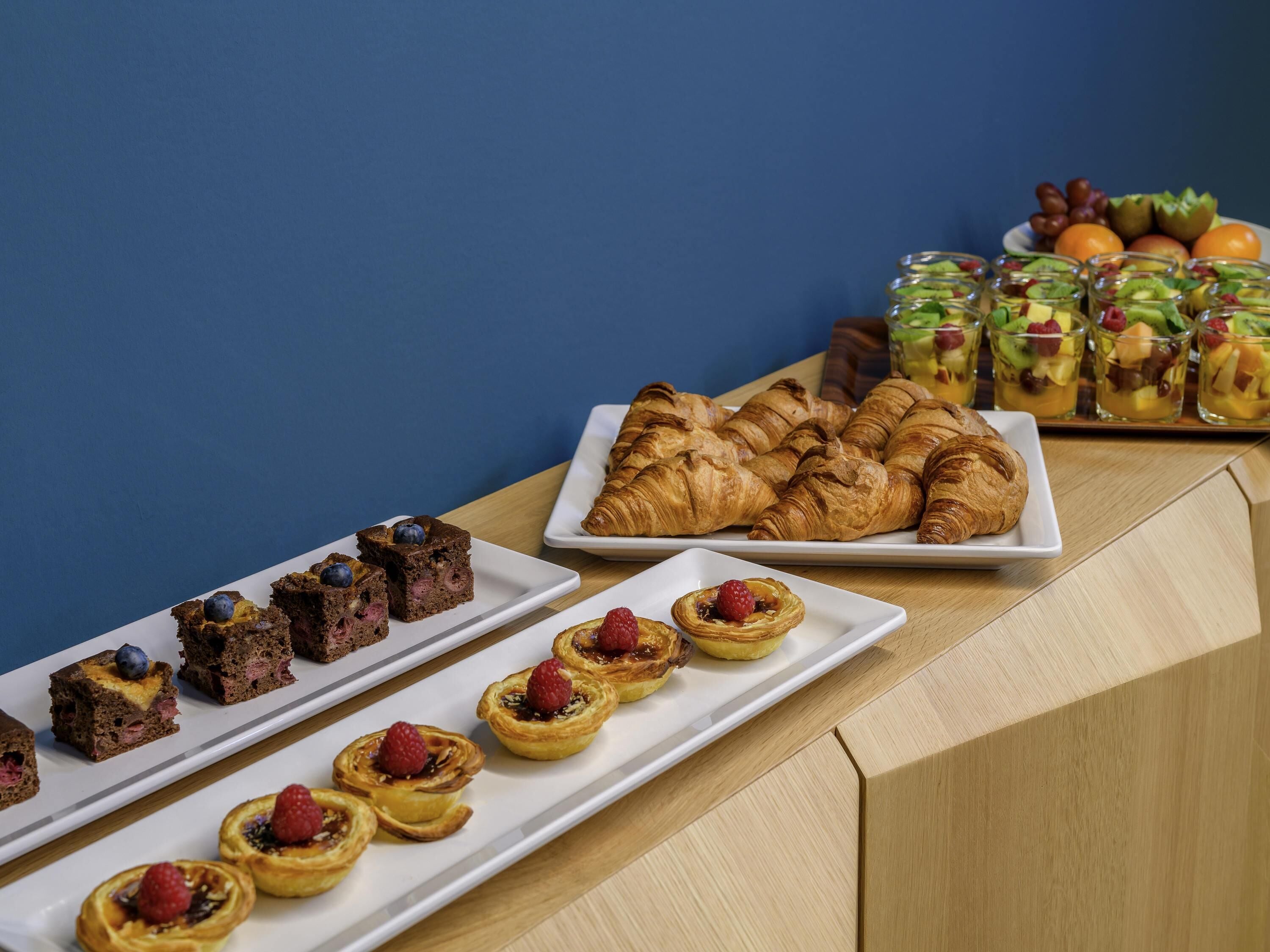 A variety of pastries and desserts on a wooden table against a blue background.