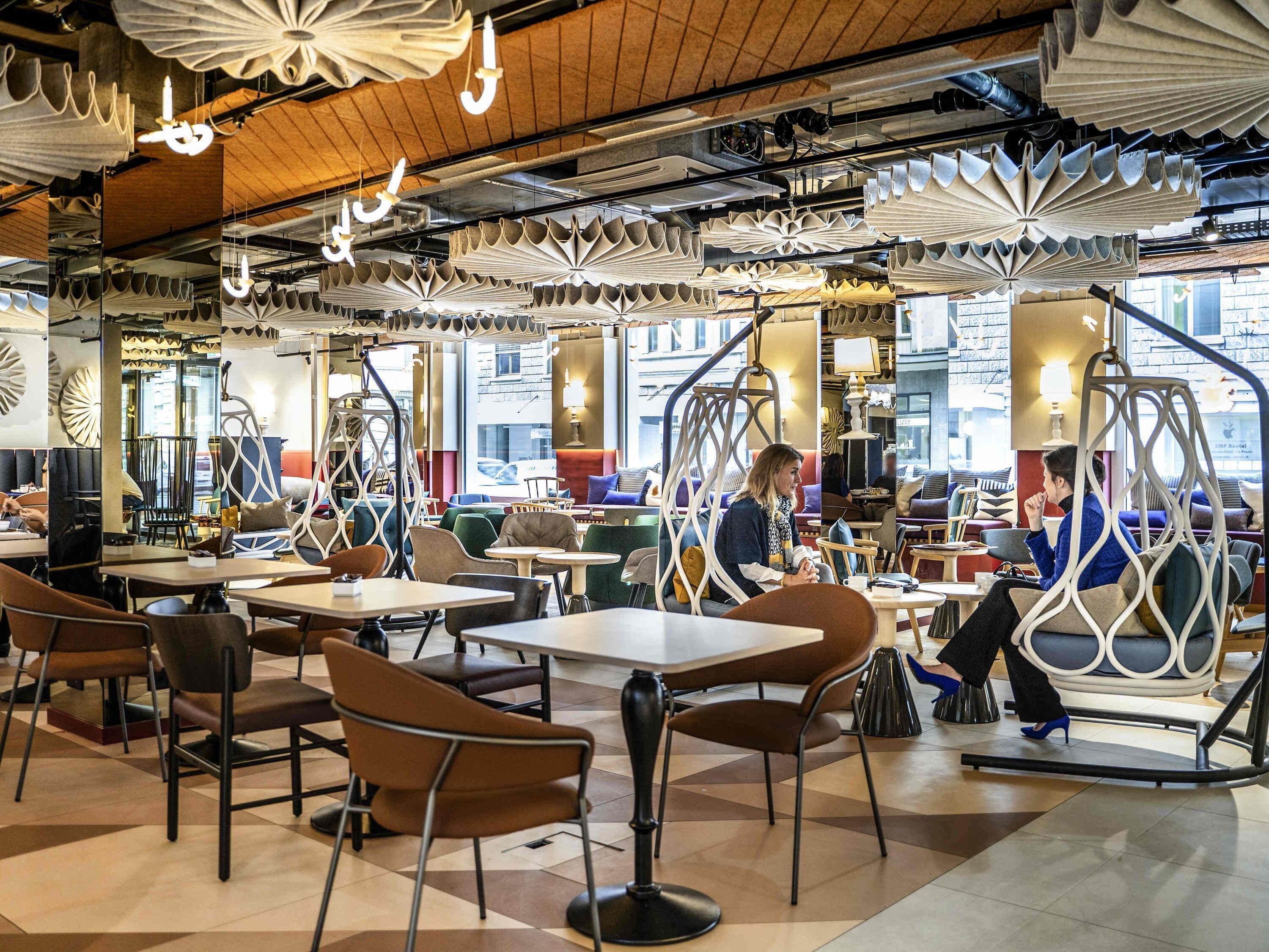 A modern cafe interior with multiple seating areas, including tables and chairs, and hanging paper lanterns.