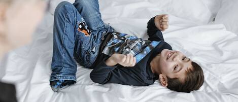 A person lying on a bed with white bedding.