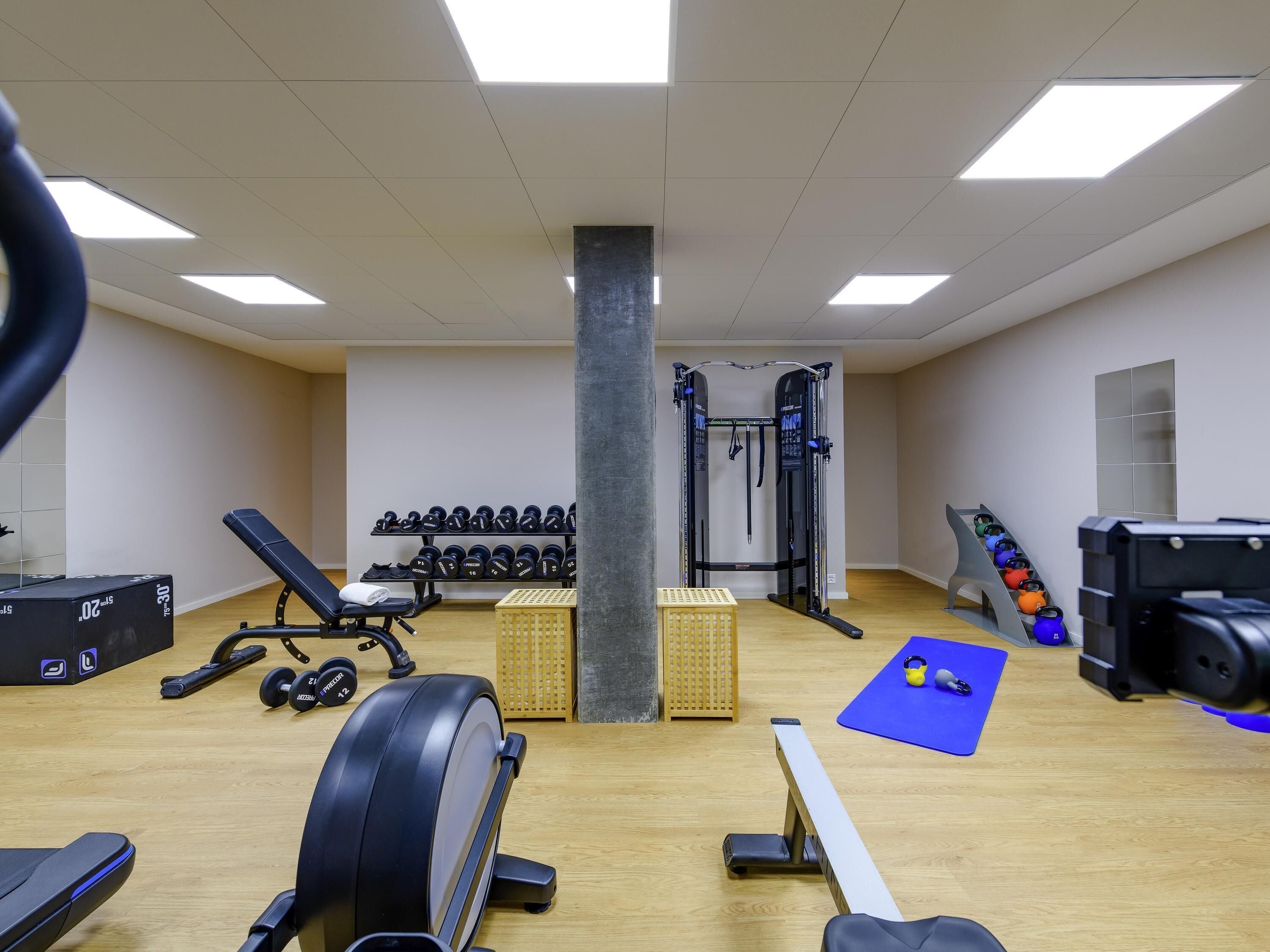 Academia com equipamentos de ginástica, pesos e um tapete azul.