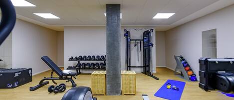 Academia com equipamentos de ginástica, pesos e um tapete azul.