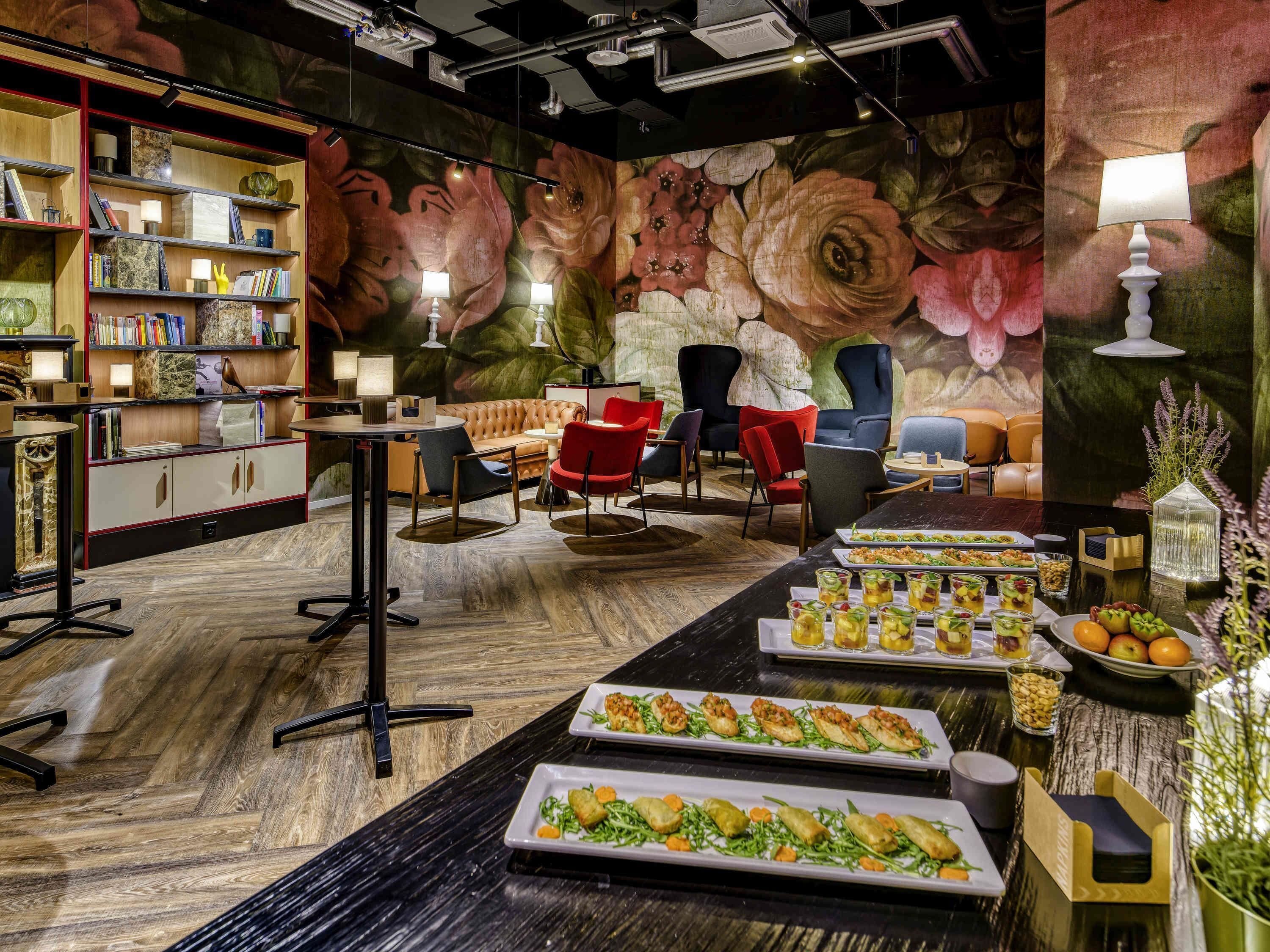 A restaurant with a long table set for a meal, a bookshelf, and a mural on the wall.