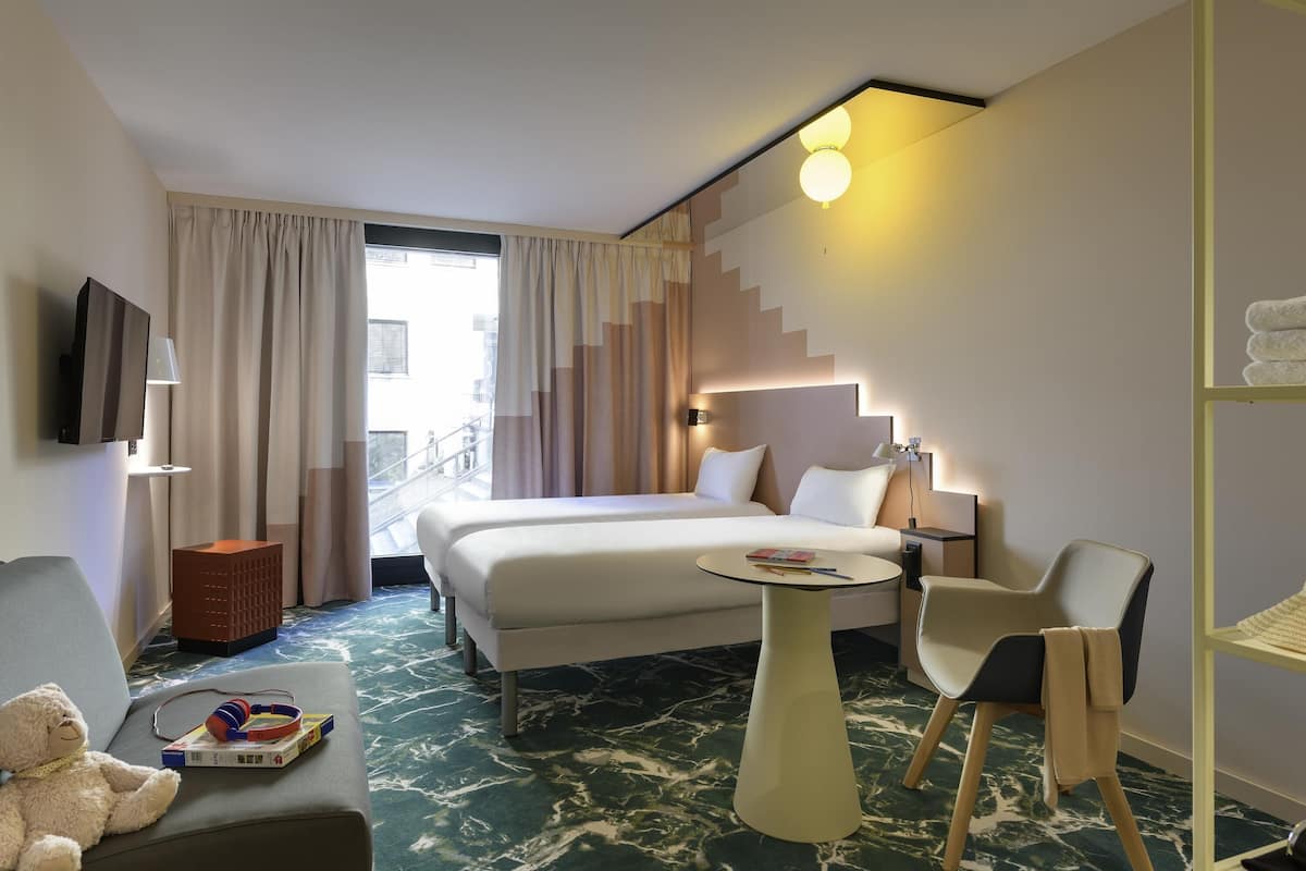 A hotel room with a bed, a sofa, a small table, a chair, a TV, and a staircase.