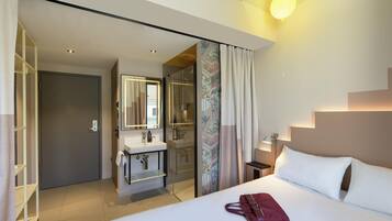 A modern hotel room with a bed, bedside table, and a bathroom with a shower.