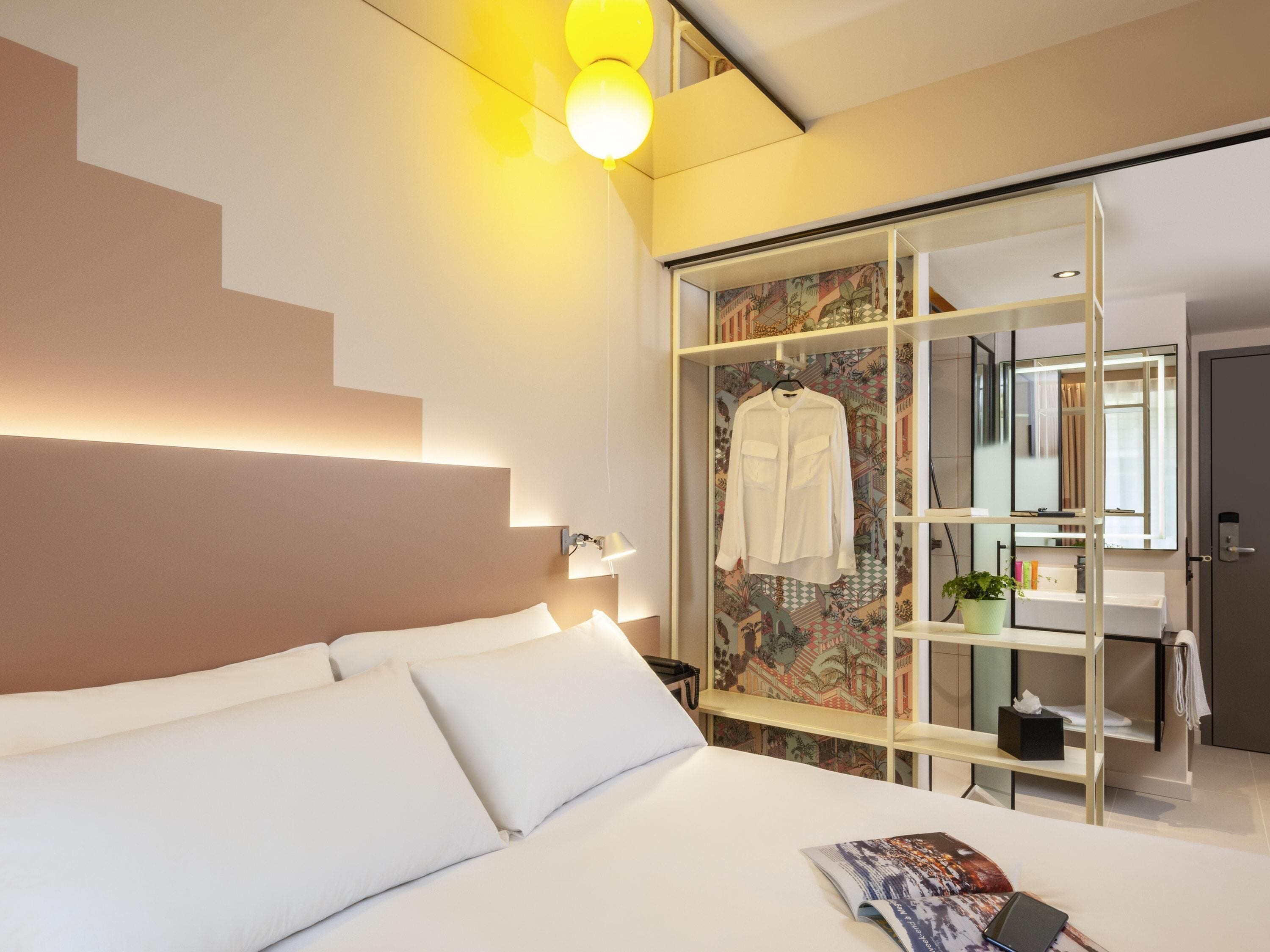 A hotel room with a bed, a bedside table, a mirror, and a wardrobe with a patterned door.