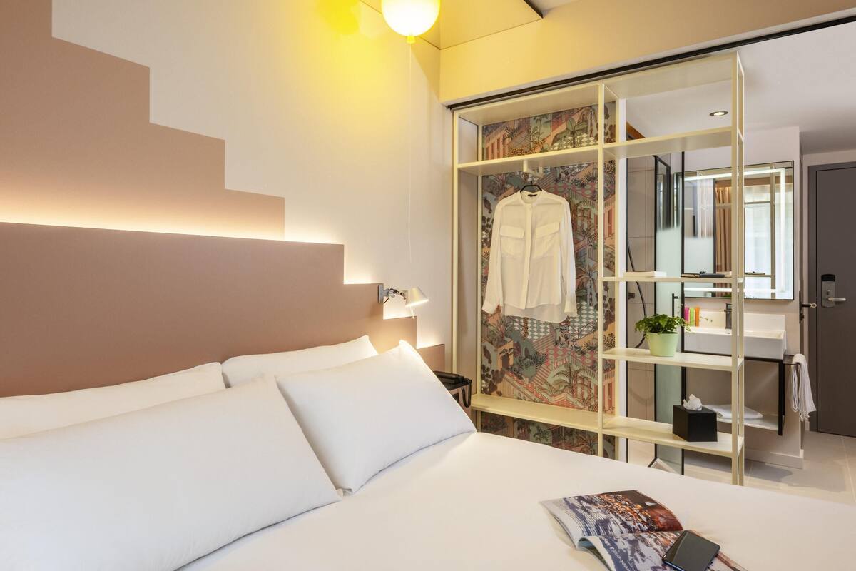 A hotel room with a bed, a bedside table, a mirror, and a wardrobe with a patterned door.