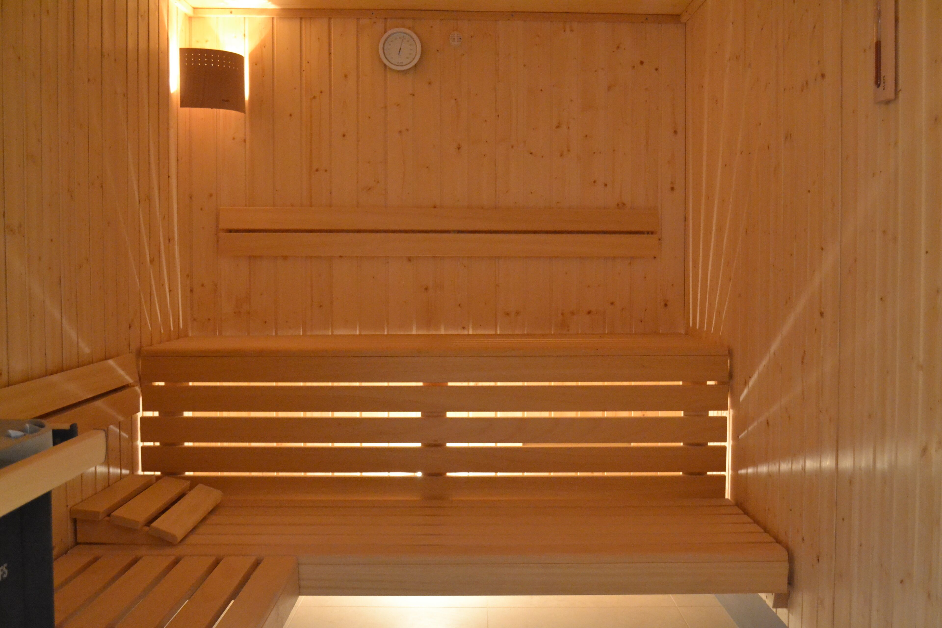 Una sauna de madera con bancos y un calentador fijado a la pared.