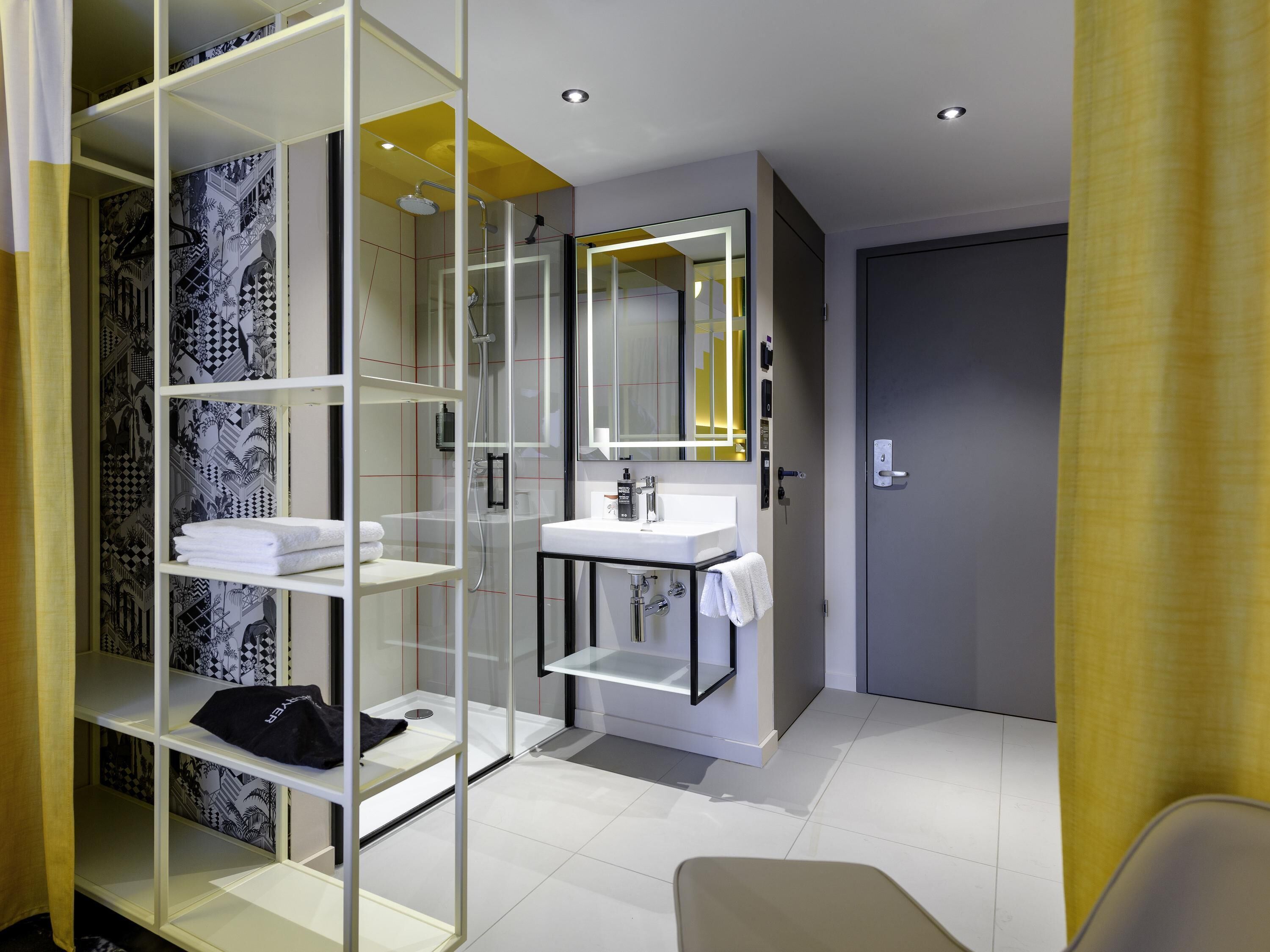 A modern bathroom with a glass shower enclosure, a white sink, and a mirror with a yellow light.