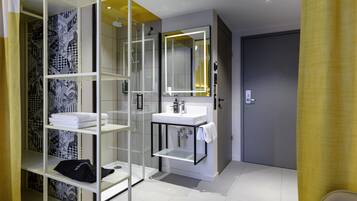 A modern bathroom with a glass shower enclosure, a white sink, and a mirror with a yellow light.