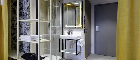 A modern bathroom with a glass shower enclosure, a white sink, and a mirror with a yellow light.