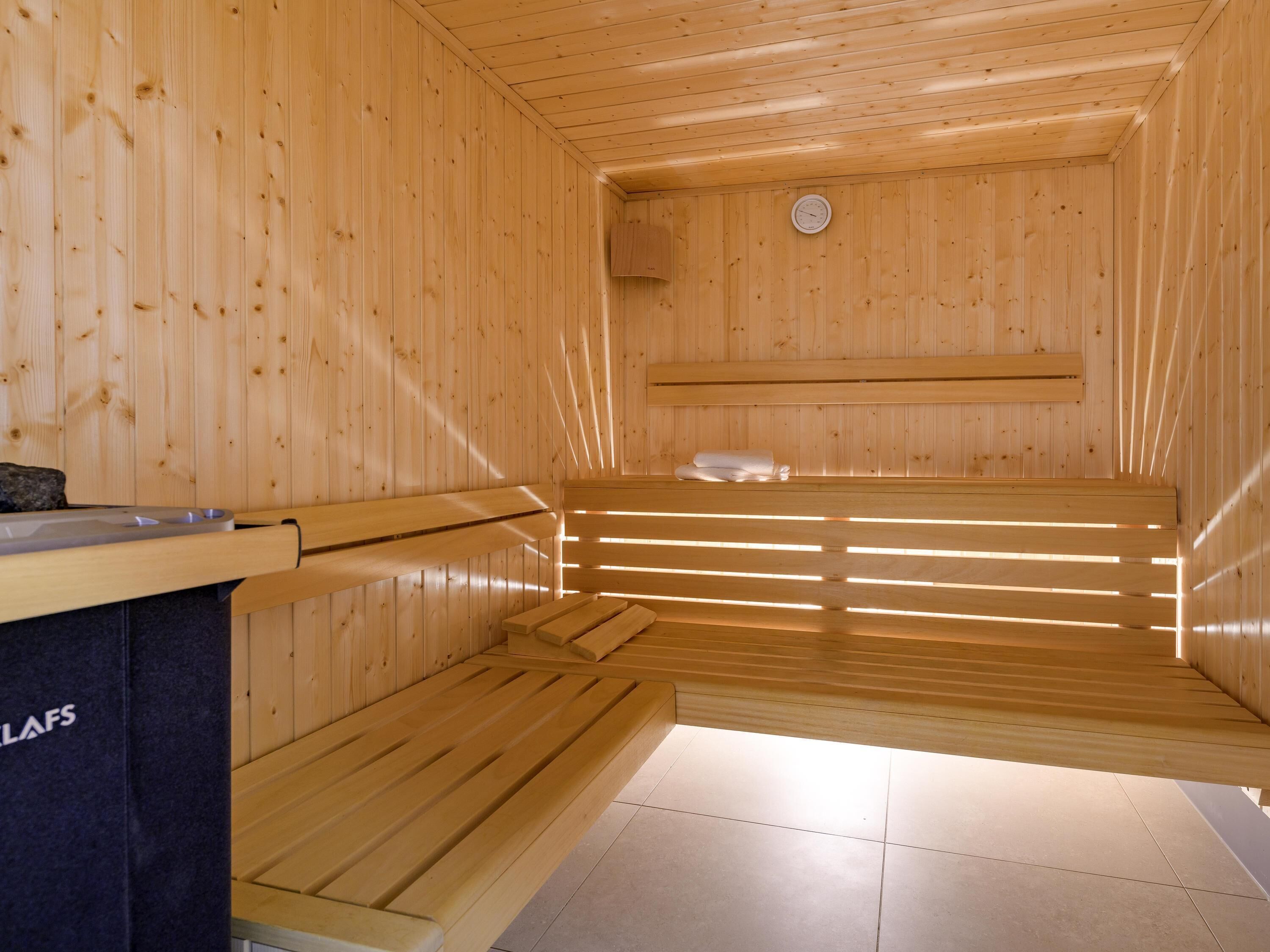 Un sauna avec des bancs en bois et une banquette, un porte-serviettes et une horloge au mur.