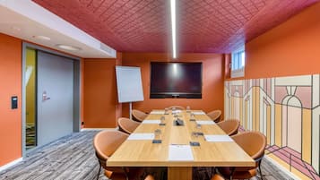 Une salle de conférence avec une longue table, des chaises, un tableau blanc et un téléviseur à écran plat fixé au mur.