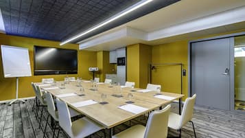 A conference room with a long table, chairs, a whiteboard, a TV, and a microwave.