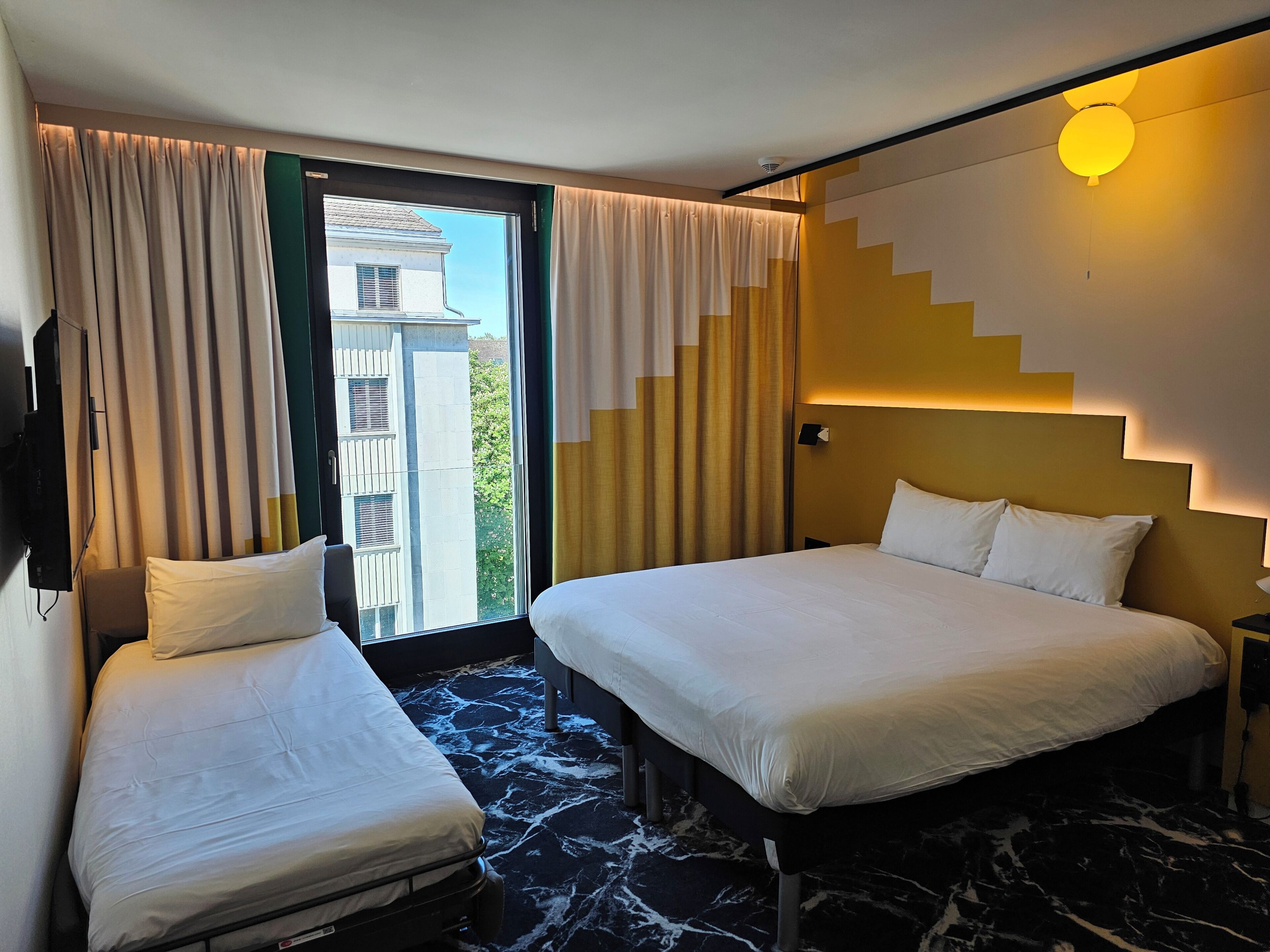 Une chambre d’hôtel avec deux lits, une grande fenêtre et une vue sur les bâtiments environnants.