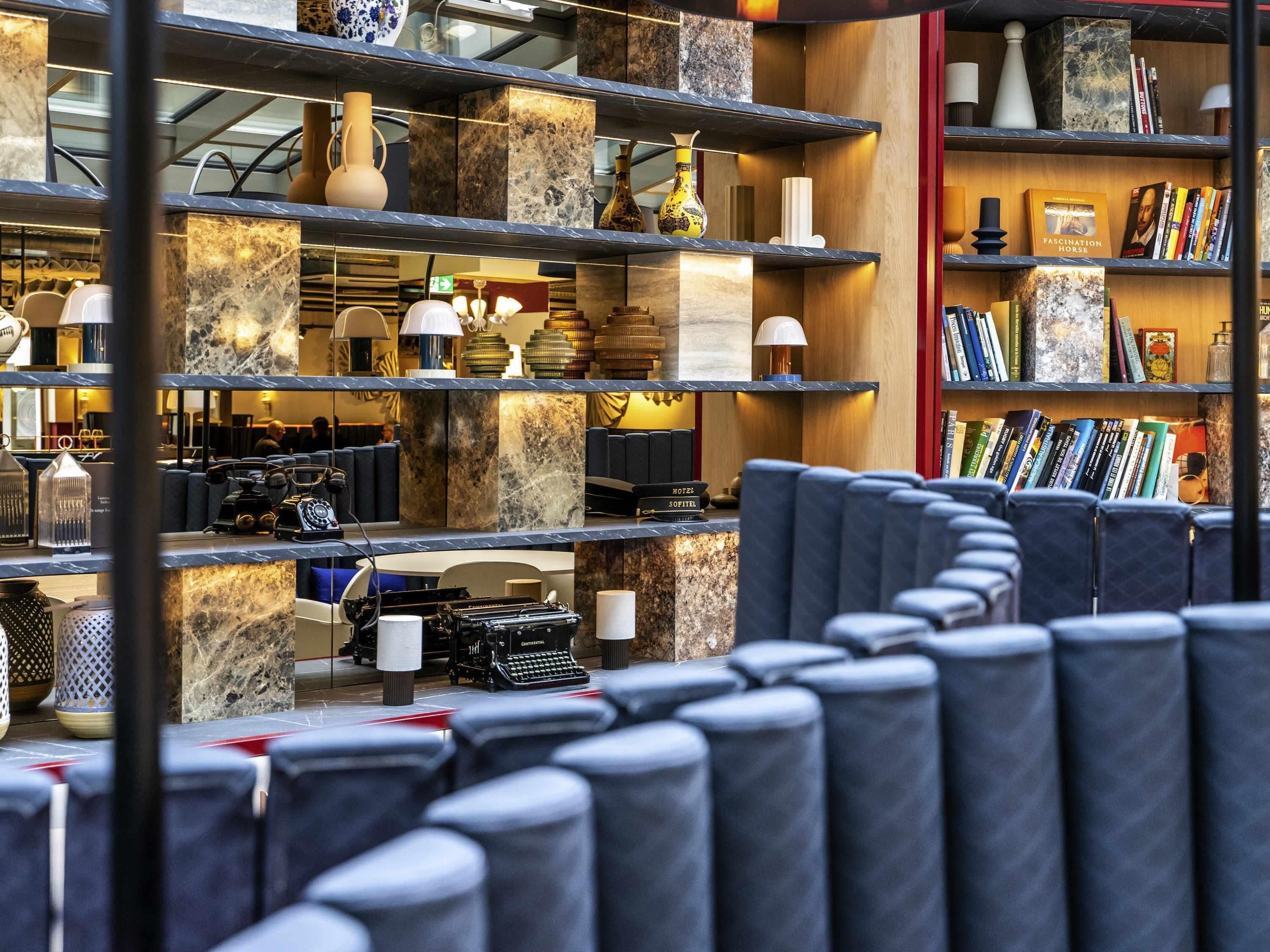 Un vestíbulo de hotel con estantes de mármol, zonas de estar y diversos objetos decorativos.
