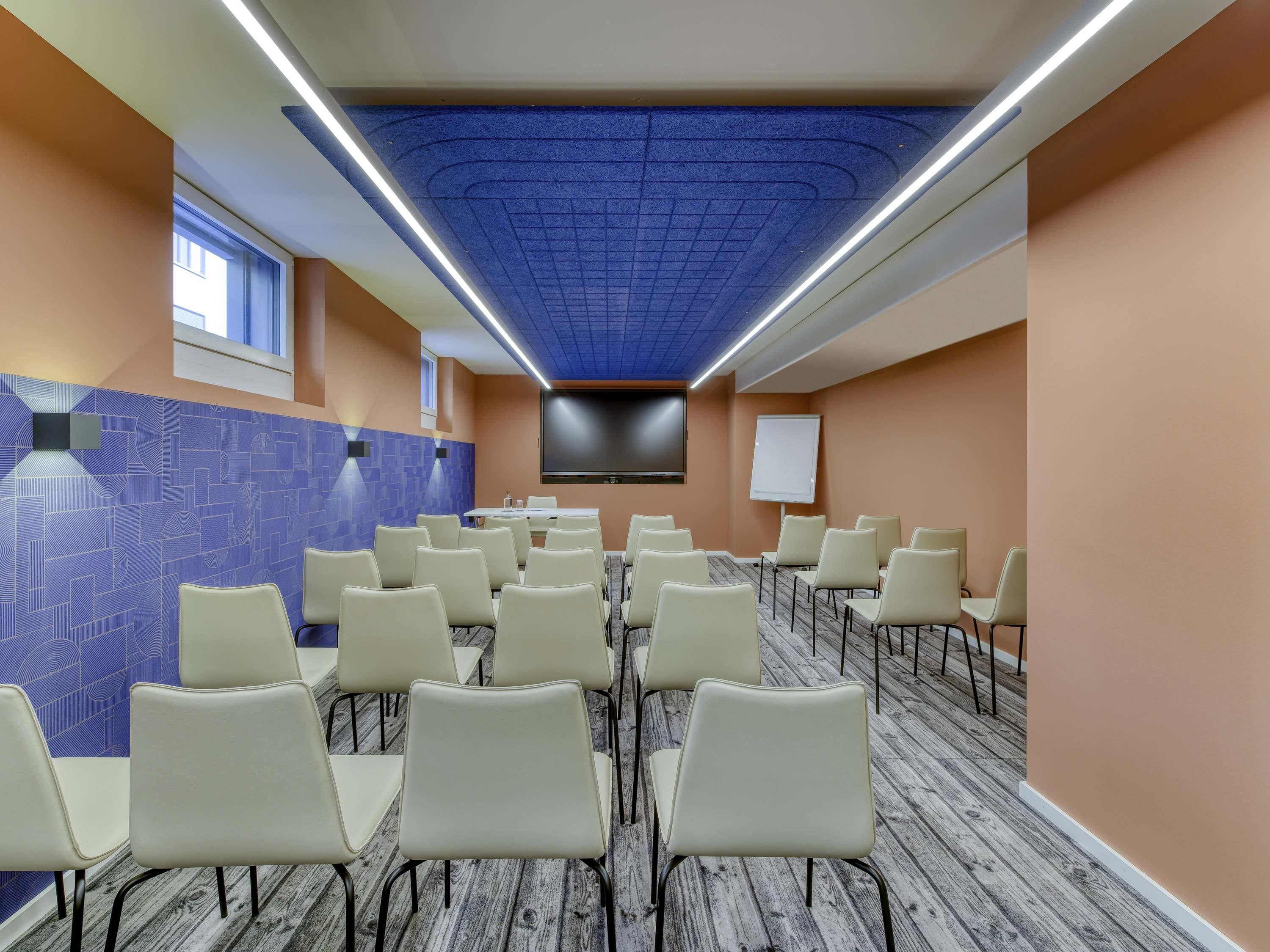 Ein Konferenzraum mit blauer Decke, einer Whiteboard und einem großen Bildschirm.