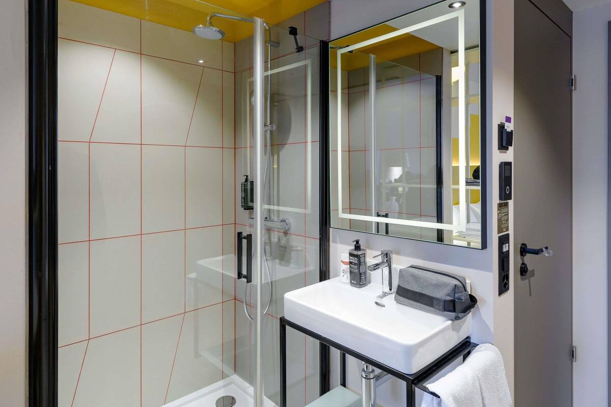 A modern bathroom with a glass shower enclosure, a white sink, and a large mirror.