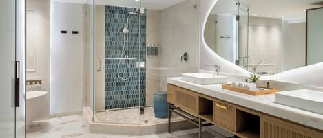 A modern bathroom with a glass-enclosed shower, two sinks, a large mirror, and a wooden vanity with towels.