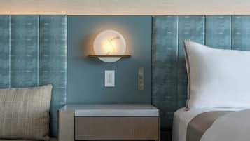 A hotel room with a bed, a nightstand, a wall-mounted light, and a textured wall panel.