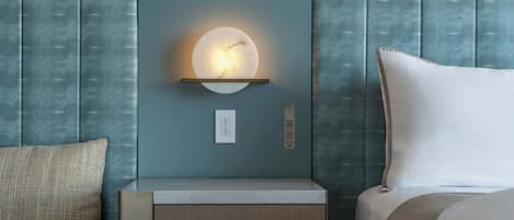 A hotel room with a bed, a nightstand, a wall-mounted light, and a textured wall panel.