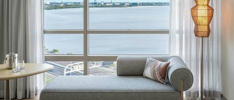 A modern room with a view of a body of water, a sofa, a table with a kettle and glass, and a floor lamp.