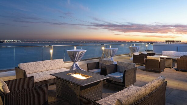 A rooftop terrace with outdoor seating, a fire feature, and a view of the city skyline at dusk.