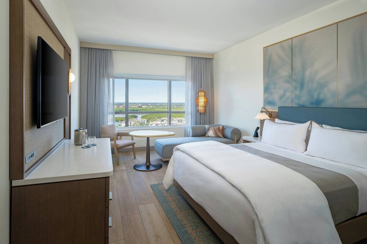 A hotel room with a bed, a desk, a TV, a window with a view, and a sofa.